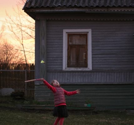 girl in red jacket and black pants standing on green grass field during daytime