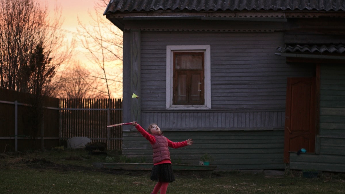 girl in red jacket and black pants standing on green grass field during daytime